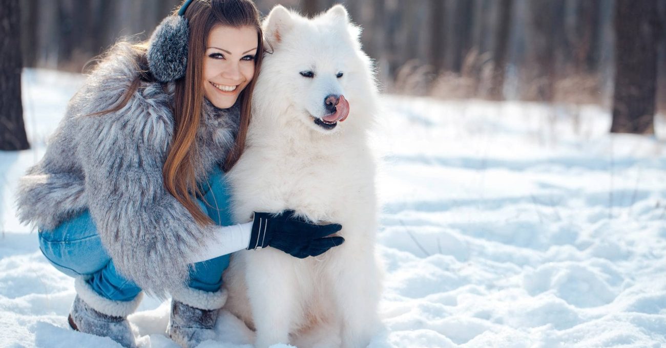 Femme souriante et chien qui se réchauffent dans la forêt en hiver pour se protéger du froid